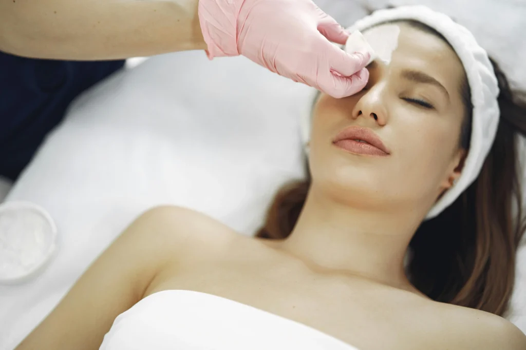 Mujer tumbada con ojos cerrados recibiendo tratamiento facial