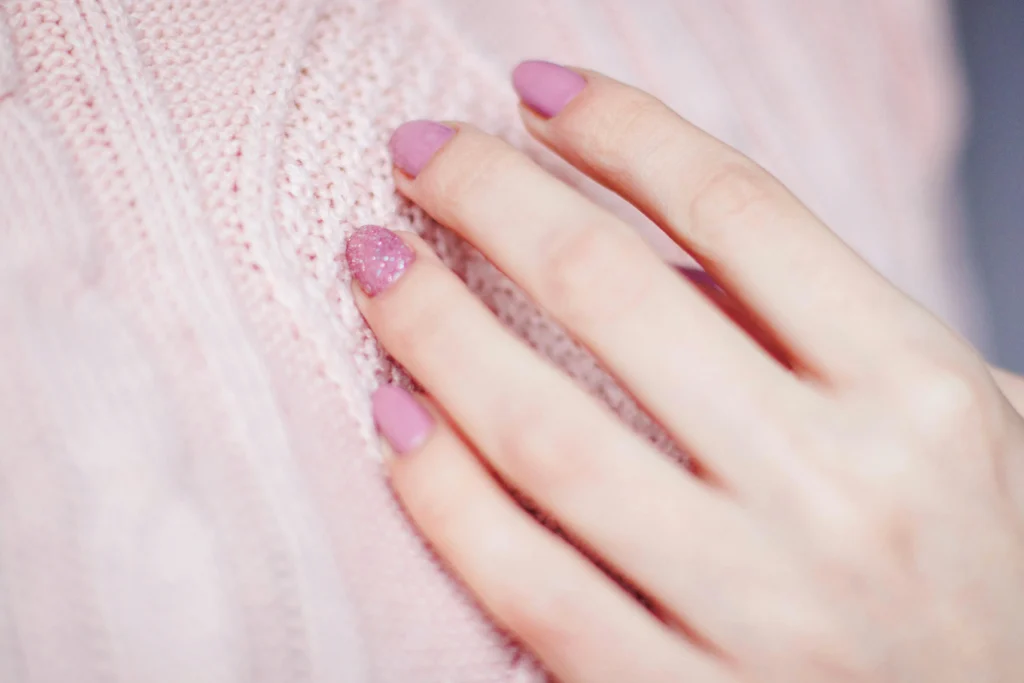 Mano con uñas pintadas en tono rosa apoyada sobre jersey rosa
