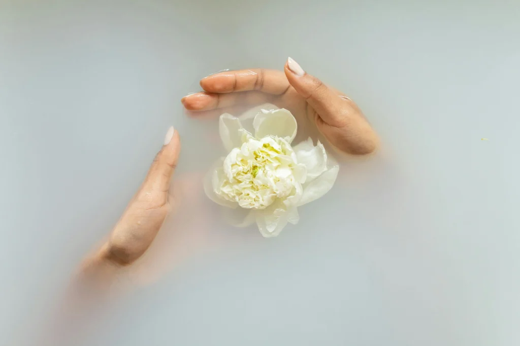 Manos sobresalen del agua y rodean una flor blanca